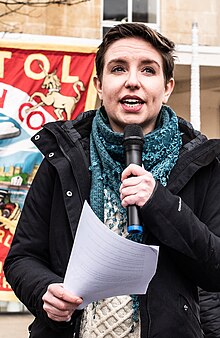 Green Party of England and Wales co-leader Carla Denyer speaking at a demonstration on the cost-of-living crisis in 2022 Carla Denyer speaking at a demonstration on the Cost of Living Crisis (cropped).jpg