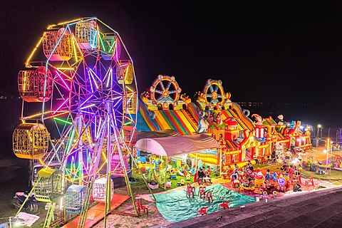 Illuminated Ferris wheel, bouncing castle and carousel at night in a funfair in Vientiane, Laos