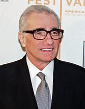 Una foto en la cabeza de un anciano con cabello gris.  Está bien afeitado y usa anteojos rectangulares.  Viste traje y corbata.