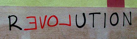 R E V O L U T I O N, graffiti with political message on a house wall. Four letters have been written backwards and with a different color so that they also form the word Love.