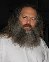 Seorang pria dengan kemeja putih dengan panjang abu-abu rambut dan jenggot panjang