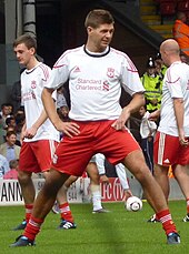 Gerrard warming up in a white jersey with red shorts and socks