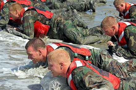 Students crawl through the surf: this intense physical and mental conditioning is used often to break down students