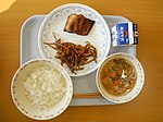 En skollunch med ris, fisk, morots- och kardborresallad, tofu- och grönsakssoppa samt mjölk.