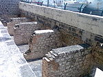 A picture of four rectangular stone structures a few feet high, laid against a wall of a larger height.