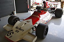 Foto van een rood-witte Formule 1 eenzitter, driekwart zicht in een beursstand.