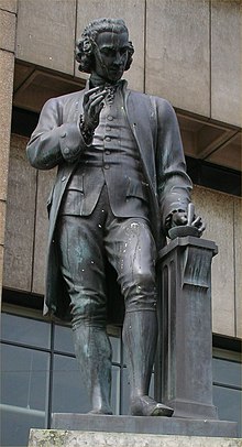 Statue of a man with a mortar and pestle in his left hand and his right hand upraised