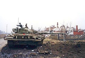 도로 바로 옆에 깔린 지뢰로 심한 피해를 입은 채 주포가 오른쪽으로 향한 유고 인민군의 M-84 전차. 배경으로 오른쪽 뒤에 파괴된 집이 있다.