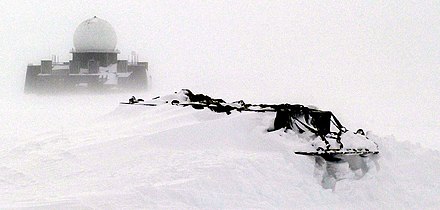 A DEW station in western Greenland is visible in the distance beyond the snow-drifted equipment pallets in the foreground of this photograph.