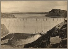 Photograph of the newly finished dam in 1916. The reservoir is partially filled. The characteristic white mineral stains on the hills are absent, as they were created during the 1942 highstand. Elephant Butte Dam LCCN2008676677.tif