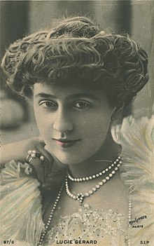 Uma fotografia em close-up, colorida à mão, de uma mulher branca com seu cabelo ondulado em um updo bufante, usando pérolas e rendas de cor clara