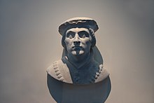 Buste en pierre d'un noble du Moyen Âge, portant un cordon autour du cou et un chapeau.