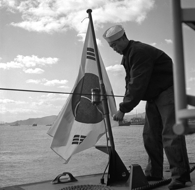 A ROKN sailor places a S. Korean naval ensign on a torpedo boat, after its transfer by the U.S. in the midst of the Korean War.