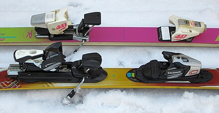 Alpine ski bindings, featuring integrated ski brakes and step-in-step-out heels (ca. 1980s, behind, 2010s, in front).