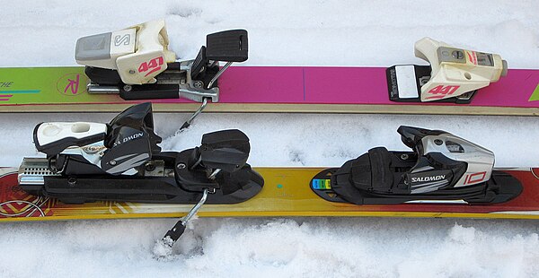 Alpine ski bindings, featuring integrated ski brakes and step-in-step-out heels (ca. 1980s, behind, 2010s, in front).