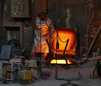 An artisan is checking on the temperature of liquid bronze before a bronze casting