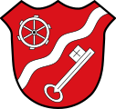 Gemeinde Kürnach In Rot ein nach links gerichteter Wellenschrägbalken, darüber ein silbernes Mühlrad, darunter ein schräglinks gestellter silberner Schlüssel.