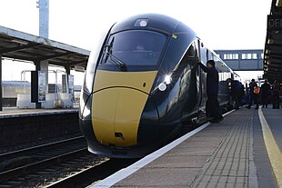 Passengers alight a large, green GWR train with a bright yellow front.