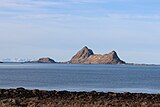 Foto zweier felsiger Inseln von der Küste aus fotografiert, weit im Hintergrund schneebedeckte Berge