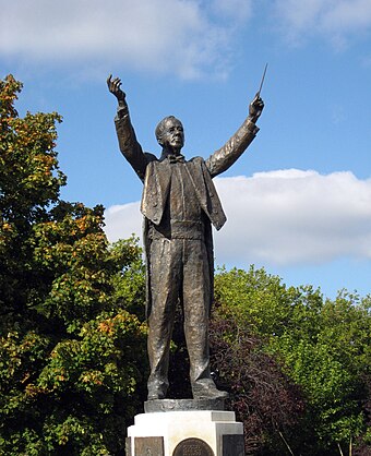 Statue of Holst at his birthplace, Cheltenham. He is shown with the baton in his left hand, his frequent practice because of the neuritis in his right arm.[43]