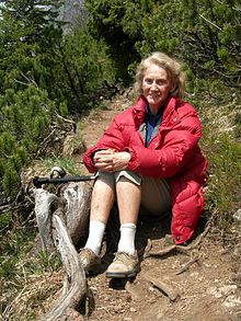 Dr. Lore Kutschera sitting on a hillside surrounded by plants, smiling at the camera