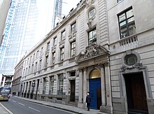 Buildings along a street. Focal point is a large blue door, number 30, flanked by 2 pillars either side, topped by a pediment with a coat of arms