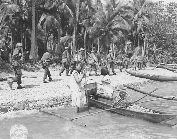 Men of the 24th Division march past Filipinos on the beach at Leyte Island.