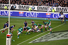 Ligne de joueurs en vert à droite, en défense, proche de sa ligne, défendant face à des adversaires en bleu.