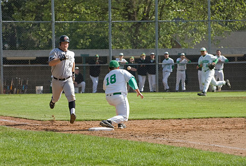 A high school first baseman takes a throw from the third baseman in an attempt to have the runner called "out".