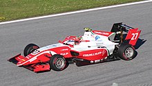 A Formula-3 fehér és piros együléses, háromnegyed nézetének fényképe felülről, egészében, egy száraz pályán.