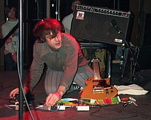 Jim O'Rourke kneeling while operating two stompboxes with his hands Jim O'Rourke-6.jpg