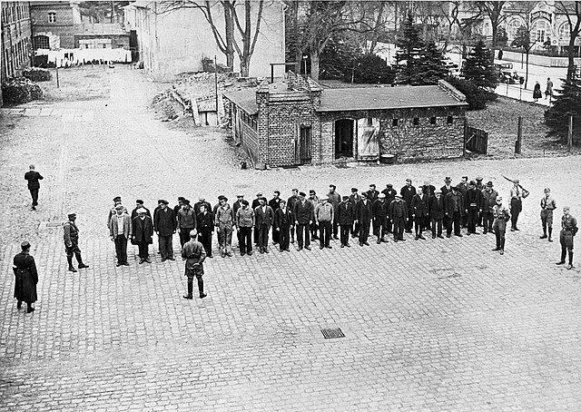 Prisoners guarded by SA men line up in the yard of Oranienburg, 6 April 1933