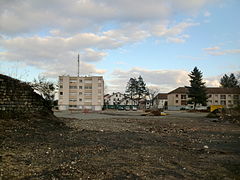 Ein leeres Grundstück mit einer Baustelle und drei Gebäuden im Hintergrund, einem Turm und zwei Bars.