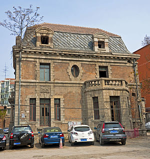 Seite des Hauses mit einem steinernen Erkerfenster im Erdgeschoss links, einer dreigliedrigen französischen Tür rechts und einer elliptischen Tür in der Mitte des Obergeschosses. Autos stehen vor.