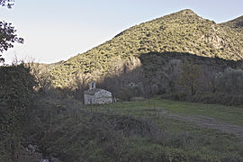 Pequeña iglesia en las sombras.  Al fondo, una pequeña montaña iluminada por el sol poniente.