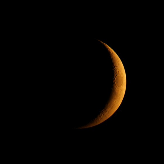 Tiefstehende, in Richtung Westen untergehende Mondsichel am 9.Oktober 2021 mit durch die Brechung des Lichts auf dem langen Weg durch die Atmosphäre bedingter grünlicher Oberkante und rötlicher Unterkante.