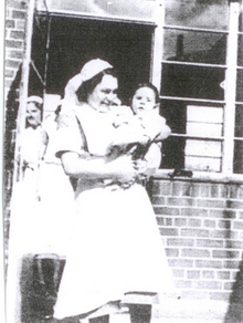 Black and white image of Alice Sluckin dresed as a nurse and holding a baby
