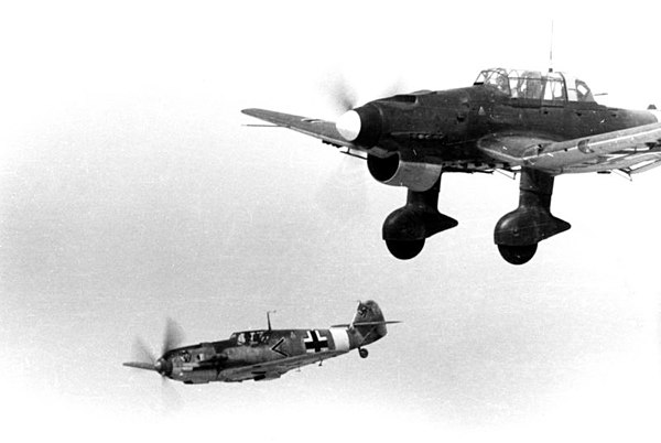 I./JG 27 Bf 109 escorts Ju 87 of StG 2, 1941. The emblem of I. Gruppe is on the cowling. The Bf 109 is probably from the Stabschwarm ("staff swarm")