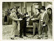 Photo en noir et blanc avec quatre personnages aux mines réjouies se tendant leurs mains droites