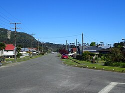 Estrada central que se estende por uma distância com bordas gramadas e edifícios em ambos os lados e um céu azul brilhante