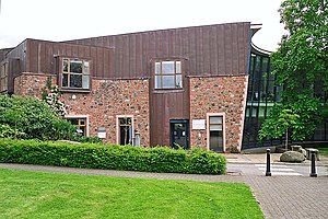 the entrance to a modern building incorporating red sandstone and large glass windows, with grass in foreground