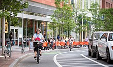 Class IV separated bike way in Cambridge, Massachusetts, the physical division for this particular bike way is the line of parked cars. Older woman with flowers protected bike lane boston.jpg