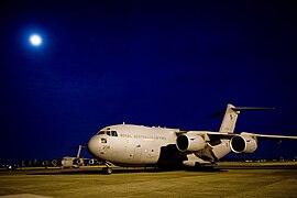Four-engined military jet transport plane parked on airfield at night with moon overhead