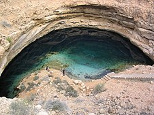 Doline dans un sol rocheux, avec une étendue d'eau en son fond.