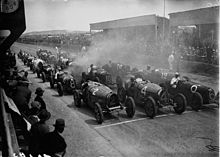 Fotografie startovního roštu Grand Prix, kde jsou vozy v těsné formaci ve třech řadách.