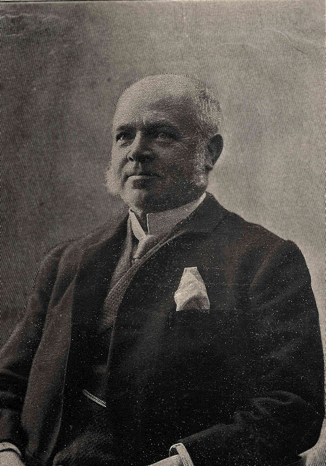 An old man with white hair and sideburns wearing a suit