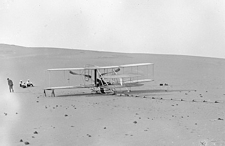 The Wright Flyer III in its two-seat configuration at the Kill Devil Hills, May 1908.  Take-offs were made from the monorail launch track; the catapult and derrick were not used.  This is the only surviving Wright brothers photo of the airplane in this configuration.  A news photographer took a picture of the aircraft in flight from a distance, but very few details are visible.