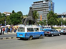 Blue and white minibus near Arat Kilo Addis Ababa street scene with the Lion of Judah Monument (Maurice Calka).jpg