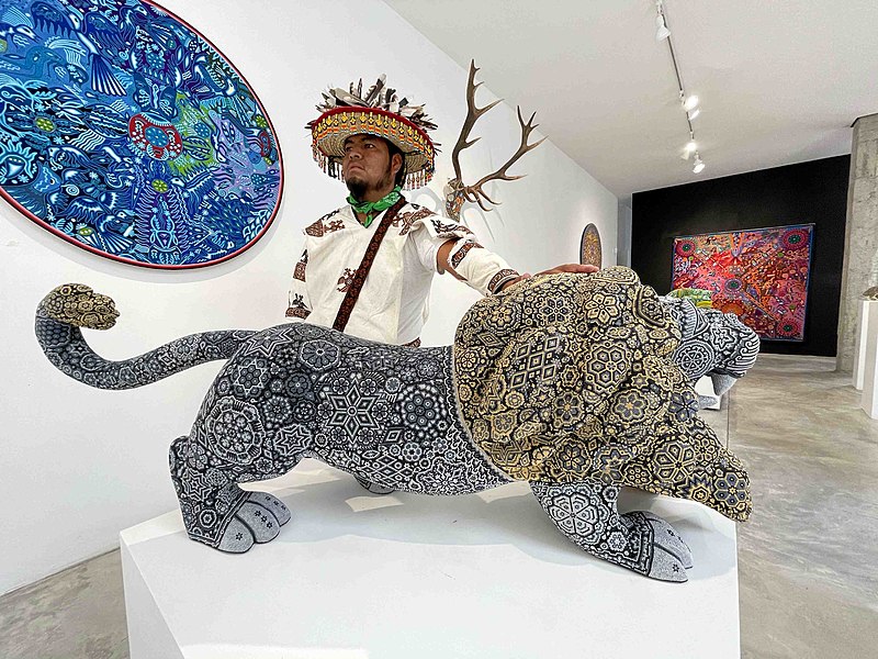 File:Artista wixárika con escultura de león intervenida con arte tradicional en micro chaquira de cristal..jpg