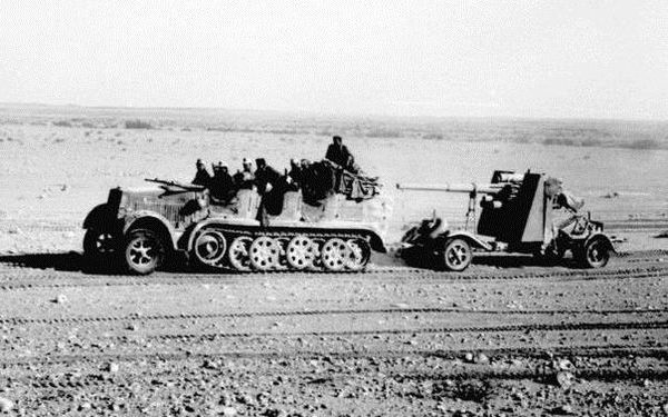 North Africa, 8.8cm Flak 18 towed behind a Sd.Kfz. 7, with its side outriggers lifted for transport visible behind the gun shield